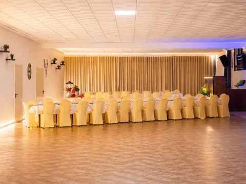 La sala interna allestita per un ricevimento: tavolata imperiale con coprisedie chiari, controsoffitto a pannelli, tendaggio lungo la parete di fondo e pavimento sgombro in primo piano.